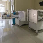 Quarto de hospital com equipamento da Câmara Hiperbárica com uma enfermeira em pé ao lado de um paciente deitado no equipamento