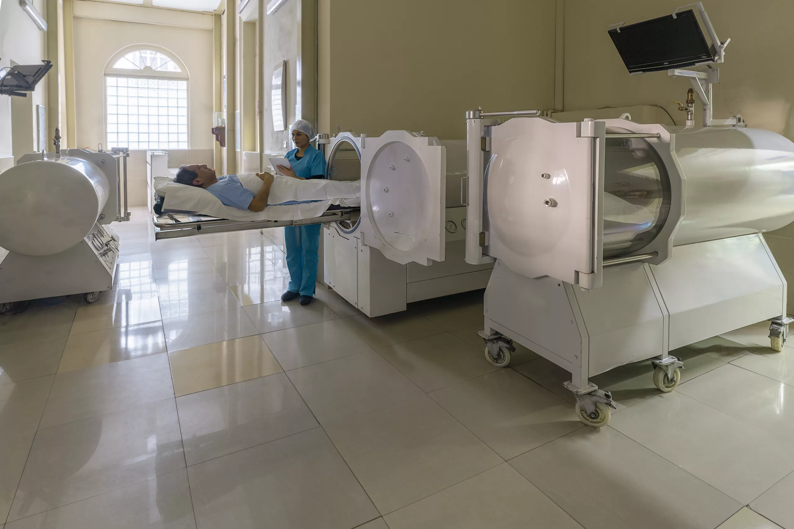 Quarto de hospital com equipamento da Câmara Hiperbárica com uma enfermeira em pé ao lado de um paciente deitado no equipamento